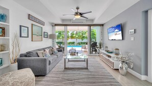 A modern living room with a gray sofa, a glass coffee table, and a ceiling fan. - Steps from Beach | Heated Pool | Gulf Stream Key | RESlDENCES (Fort Lauderdale)