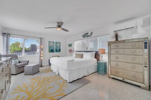 Une chambre à coucher comprenant un lit, une commode, une chaise, un ventilateur de plafond et une fenêtre avec des stores.