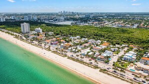 An aerial view of a coastal town with a beachfront, residential buildings, and a marina. - Steps from Beach | Heated Pool | Gulf Stream Key | RESlDENCES (Fort Lauderdale)