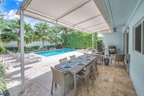 An outdoor patio with a pool, dining table, chairs, and a grill area. - Steps from Beach | Heated Pool | Gulf Stream Key | RESlDENCES (Fort Lauderdale)