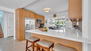 A modern kitchen with wooden cabinets, a large island with stools, stainless steel appliances, and a view to the living area. - Steps from Beach | Heated Pool | Gulf Stream Key | RESlDENCES (Fort Lauderdale)