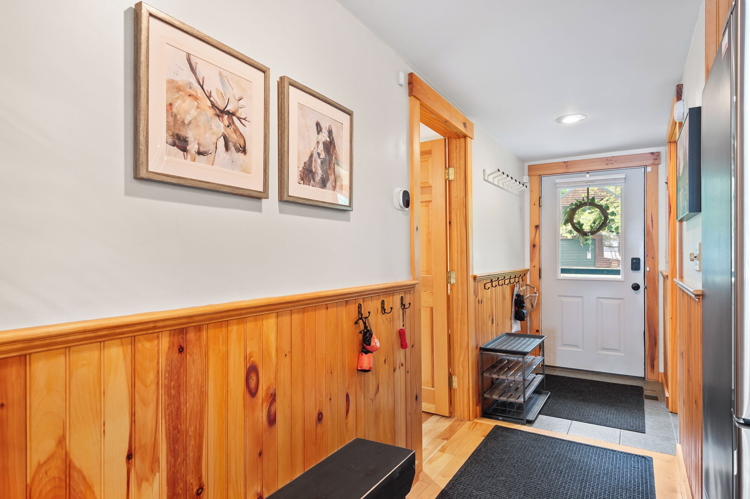 A hallway with wooden paneling, a bench, a coat rack, and two framed pictures on the wall.