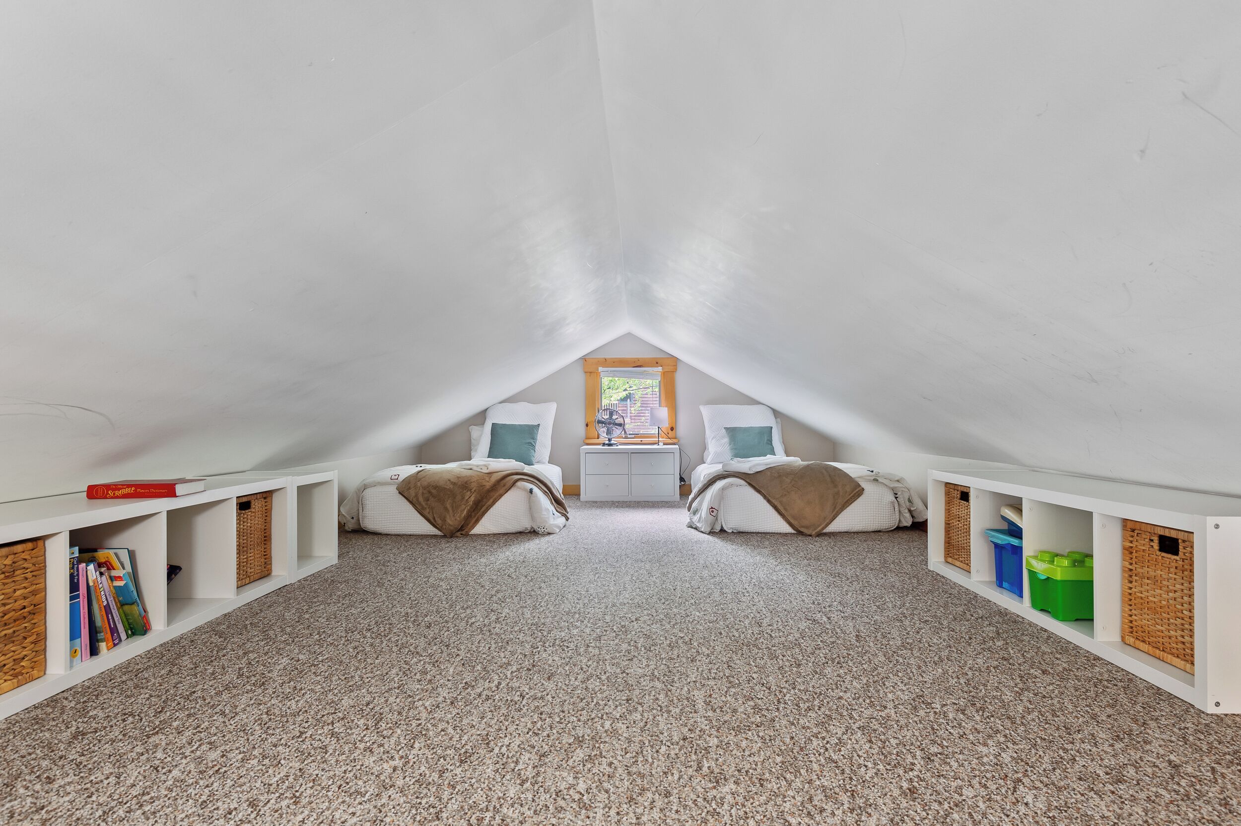 An attic bedroom with two beds, a nightstand, and built-in storage.