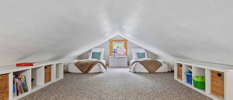 An attic bedroom with two beds, a nightstand, and built-in storage.