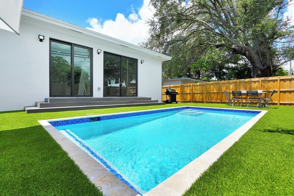 Une maison moderne dotée d’une piscine, d’une terrasse en bois et d’un grand arbre.