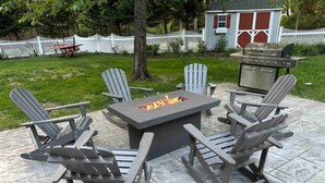 En uteplats med Adirondack-stolar, en rektangulär eldstad och en grill.