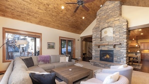 A spacious living area with a stone fireplace, wooden ceiling, and a large sectional sofa. - Luxury 4,200 sq ft duplex perched above Breckenridge overlooking the 10-mile range! (Breckenridge)