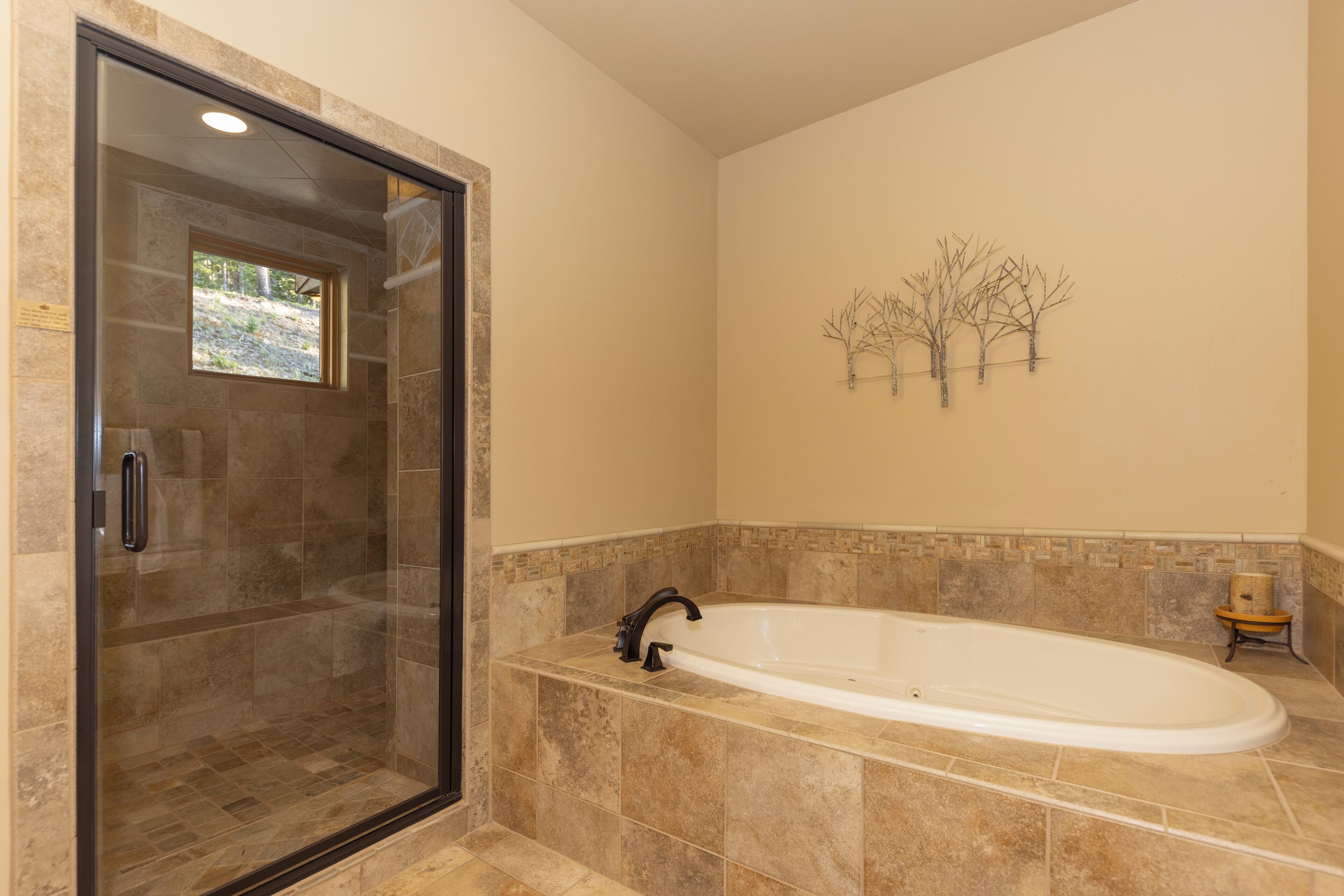 A bathroom with a glass-enclosed shower, a freestanding bathtub, and a decorative tree wall art piece.