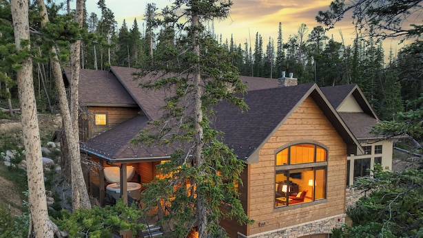 A log cabin with a stone foundation, a large window, and a visible hot tub area. - Luxury 4,200 sq ft duplex perched above Breckenridge overlooking the 10-mile range! (Breckenridge)