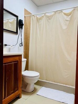 Ein Badezimmer mit Toilette, einem Holzschrank, einem Föhn und einem beige farbenen Duschvorhang.