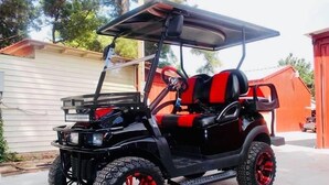 Un carrito de golf negro con detalles rojos y neumáticos grandes para terrenos difíciles estacionado en una entrada.