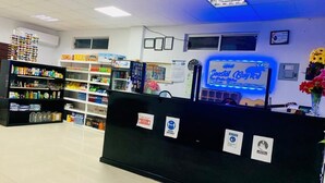 Interior de una farmacia con un mostrador de recepción, estantes llenos de diversos productos y una pantalla digital que anuncia Coastal Breeze.