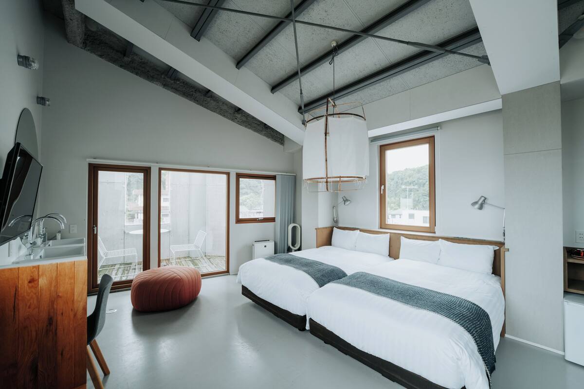 A modern bedroom with a large bed, a wooden desk, and a view of the city through large windows.
