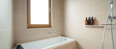 A modern bathroom with a bathtub, a shower, and a window.