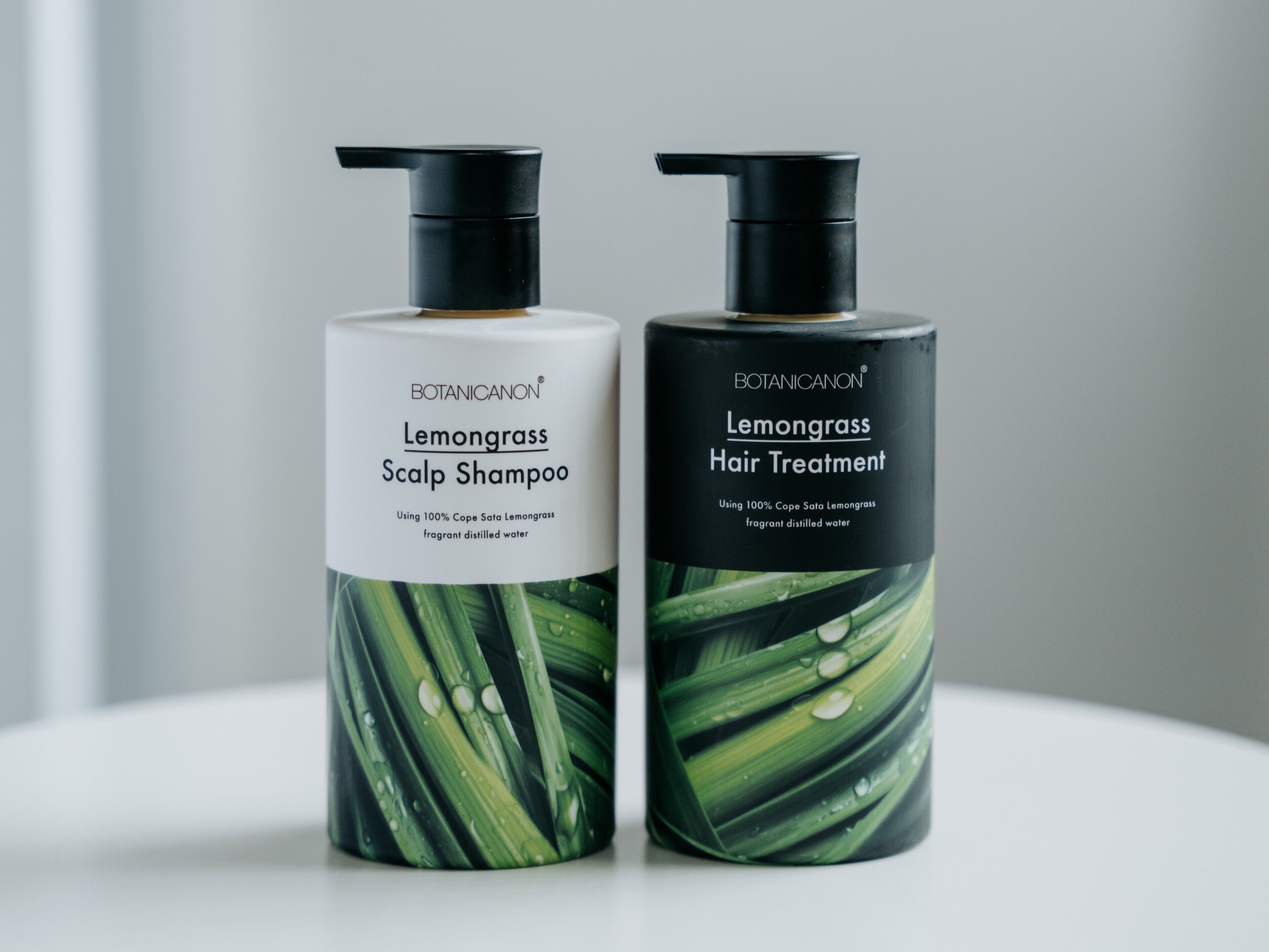 Dos botellas de productos Lemongrass, una etiquetada como 'Scalp Shampoo' y la otra 'Hair Treatment', ambas con dosificador tipo bomba.