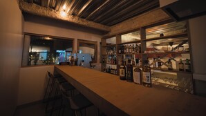 Zona de bar con una barra alargada, taburetes y estantes llenos de botellas.