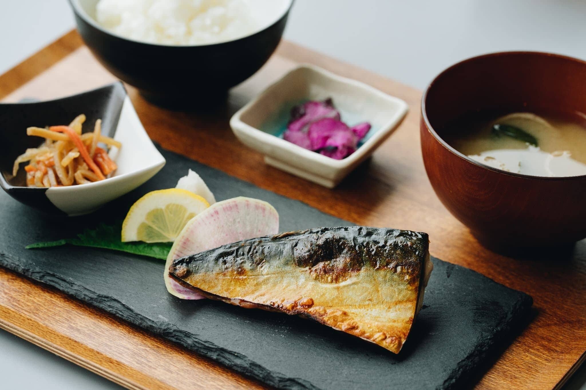 A fish dish with lemon slices and pickled vegetables on a slate board.