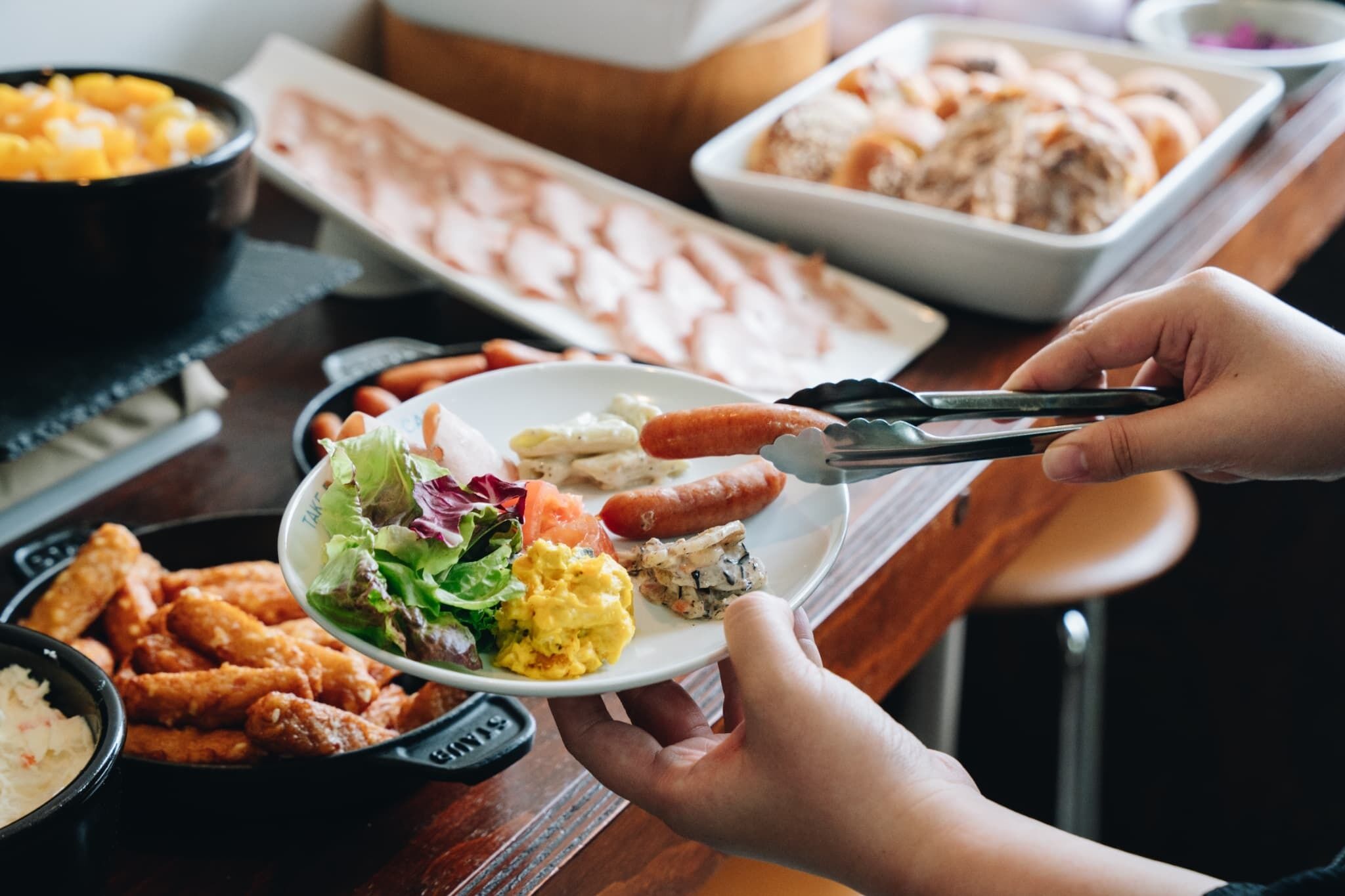 Une table à manger avec différents plats, notamment une salade, des saucisses et d’autres aliments.