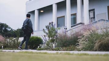 A person walking towards a modern building with large columns and a flat roof.