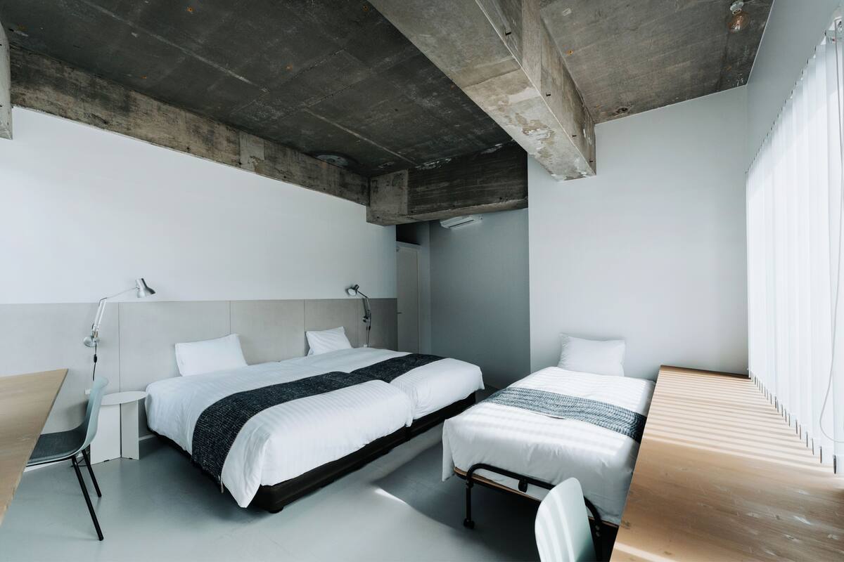 A modern hotel room with two beds, a desk, and a large window.