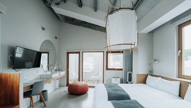 Una habitación de hotel moderna con una cama grande, un escritorio con televisor de pantalla plana, un banco de madera y un ventanal amplio.
