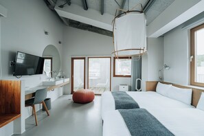 Una habitación de hotel moderna con una cama grande, un escritorio con televisor de pantalla plana, un banco de madera y un ventanal amplio.