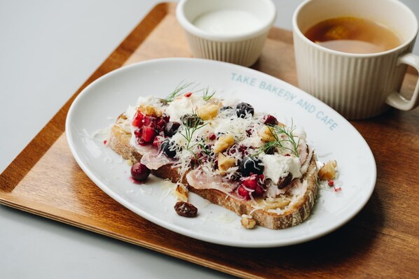 Un plato de comida con diferentes ingredientes, acompañado de una taza de té y un vasito de leche sobre una bandeja de madera.