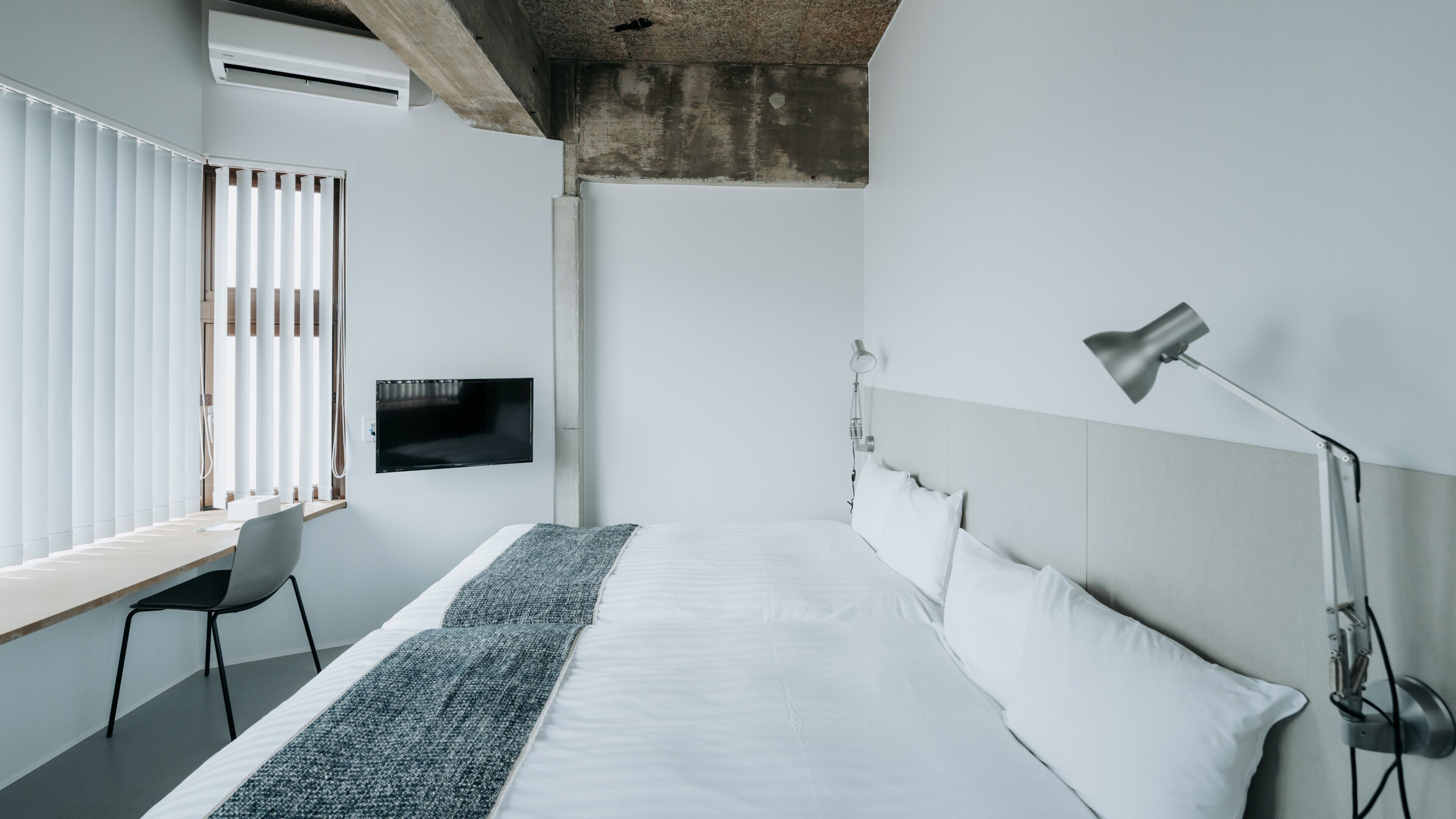 A modern hotel room with a bed, a desk, a TV, and a lamp.
