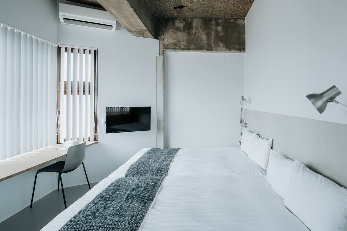 A modern hotel room with a bed, a desk, a TV, and a lamp.