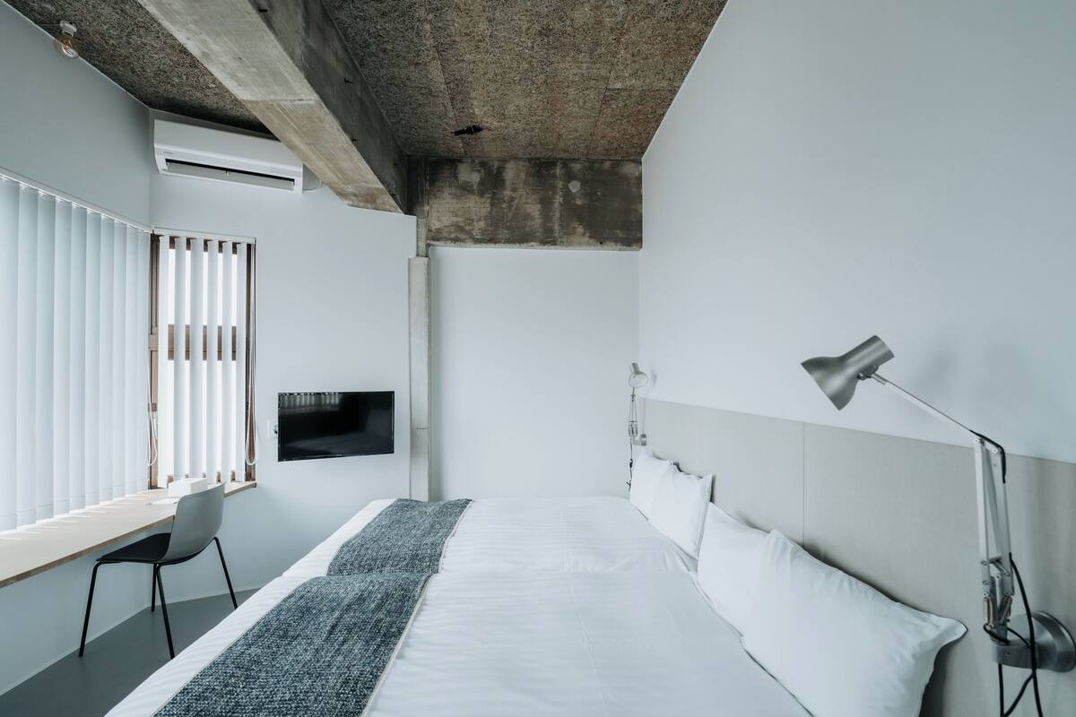 A modern bedroom with a bed, a desk, a chair, a TV, and a lamp.