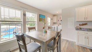 Una cocina con armarios blancos, una mesa de comedor con sillas, vista a una piscina y un cuadro en la pared.