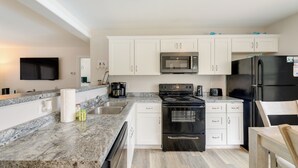 Una cocina moderna con armarios blancos, encimera de granito, estufa negra, microondas y refrigerador.