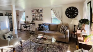 Een woonkamer met een bank, fauteuils, een salontafel, een vloerkleed, een klok en ingelijste foto's aan de muur.