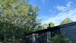 Een houten terras met een barbecue, een overdekte zithoek en een klein portaaltje met lichtjes.