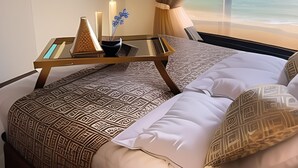 A hotel room with a bed, a bedside table with decorative items, a wall-mounted TV, and a view of the beach through a window. - My Sky • Wake to the Sea • Quiet Coastal Apartment + Private Beach (Hurghada , Al Aheya)
