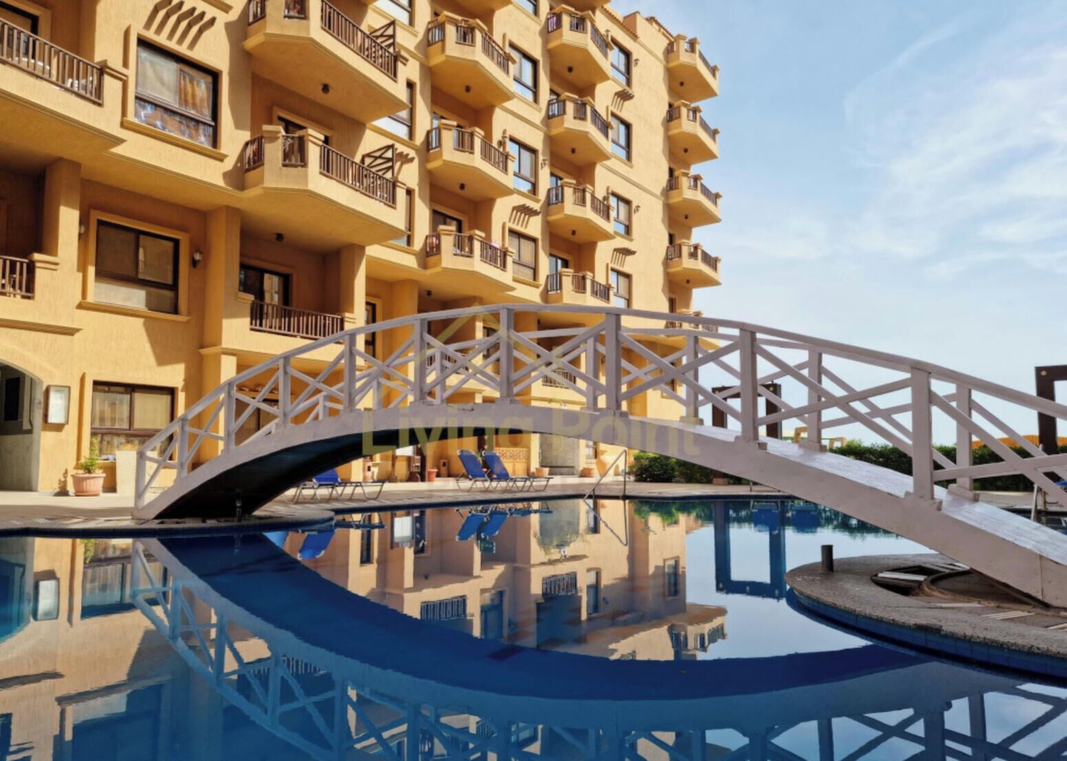 A swimming pool with a white bridge, surrounded by a multi-story building with balconies.