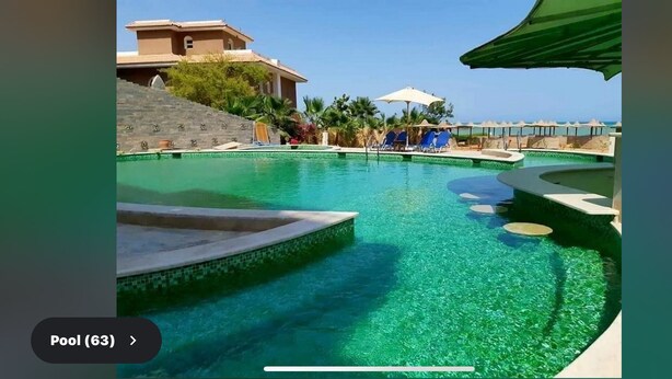 A pool area with clear water, lounge chairs, and a building in the background. - My Sky • Wake to the Sea • Quiet Coastal Apartment + Private Beach (Hurghada , Al Aheya)