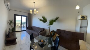 A modern living room with a glass dining table, two sofas, a chandelier, and a view through a sliding glass door to the outdoors. - My Sky • Wake to the Sea • Quiet Coastal Apartment + Private Beach (Hurghada , Al Aheya)
