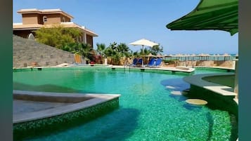 A pool area with clear water, lounge chairs, and a building in the background.