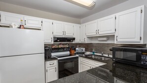 A modern kitchen with white cabinets, a black countertop, a stove, a microwave, and a toaster. - Legend Villas of Bay Point 4261 (Panama City Beach)