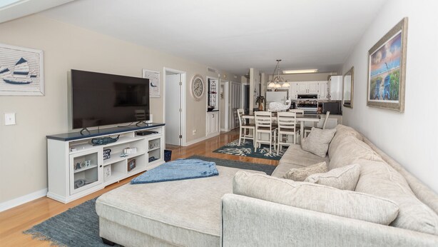 A living room with a TV, a sofa, and a dining area with chairs and a table. - Legend Villas of Bay Point 4261 (Panama City Beach)