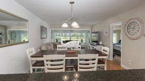 A modern kitchen with granite countertops, a dining area with white chairs, a large mirror, and a clock on the wall. - Legend Villas of Bay Point 4261 (Panama City Beach)