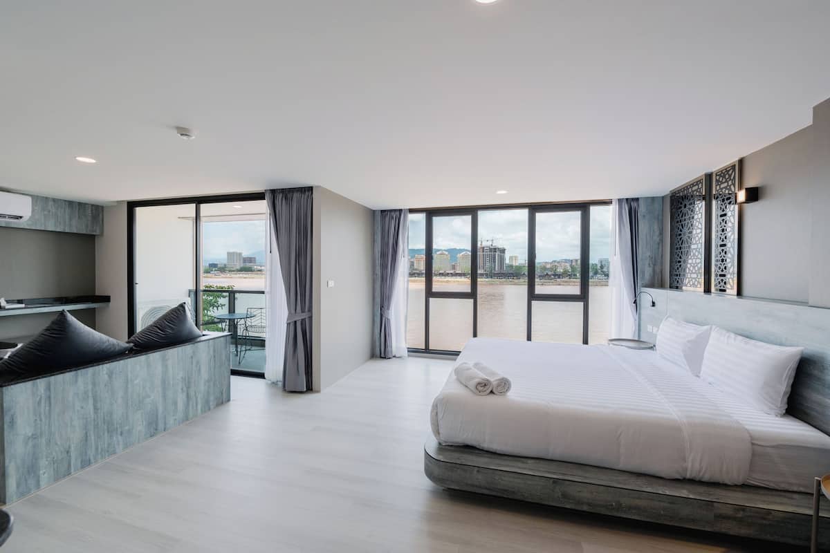 A modern hotel room with a large bed, a seating area, and a balcony with a city view.
