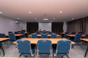 Un salón de conferencias con mesas y sillas, un proyector y una pantalla.