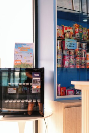 Un refrigerador para bebidas con varias opciones, una sección de snacks que solo acepta efectivo y un cartel que anuncia una bebida especial gratuita.