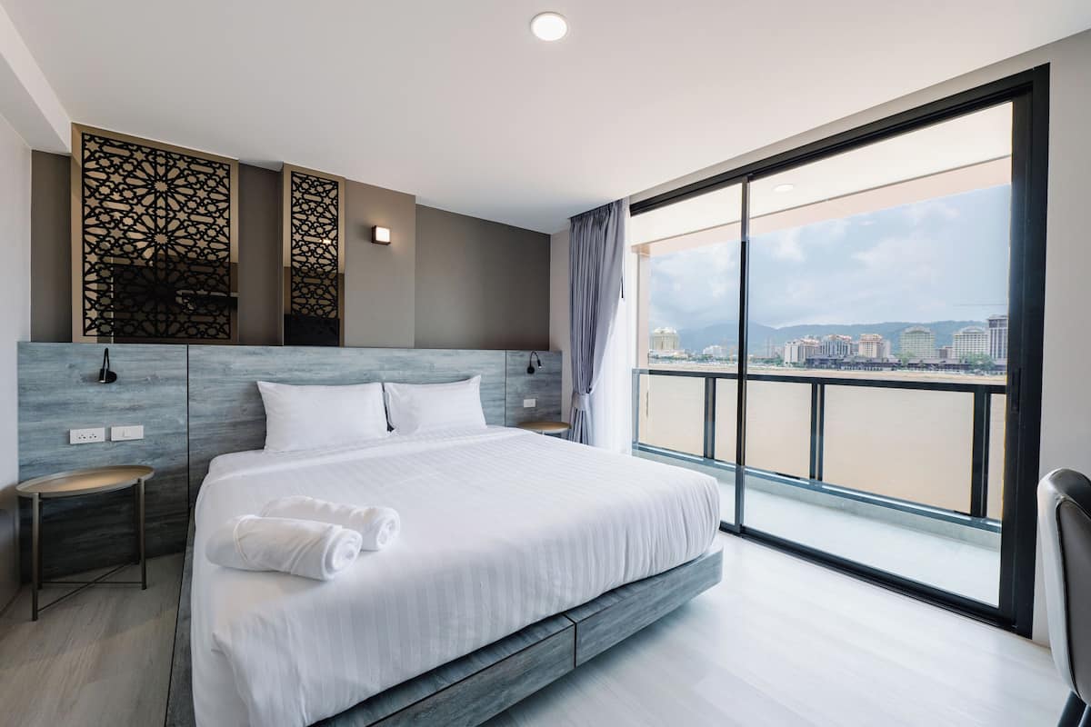 A modern hotel room with a large bed, a view of a river, and a balcony.