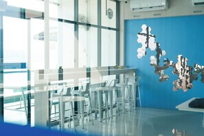 A modern interior with a glass partition, white chairs, a blue accent wall, and a Samsung air conditioner. - One Budget Chiangsaen (Chiang Saen)