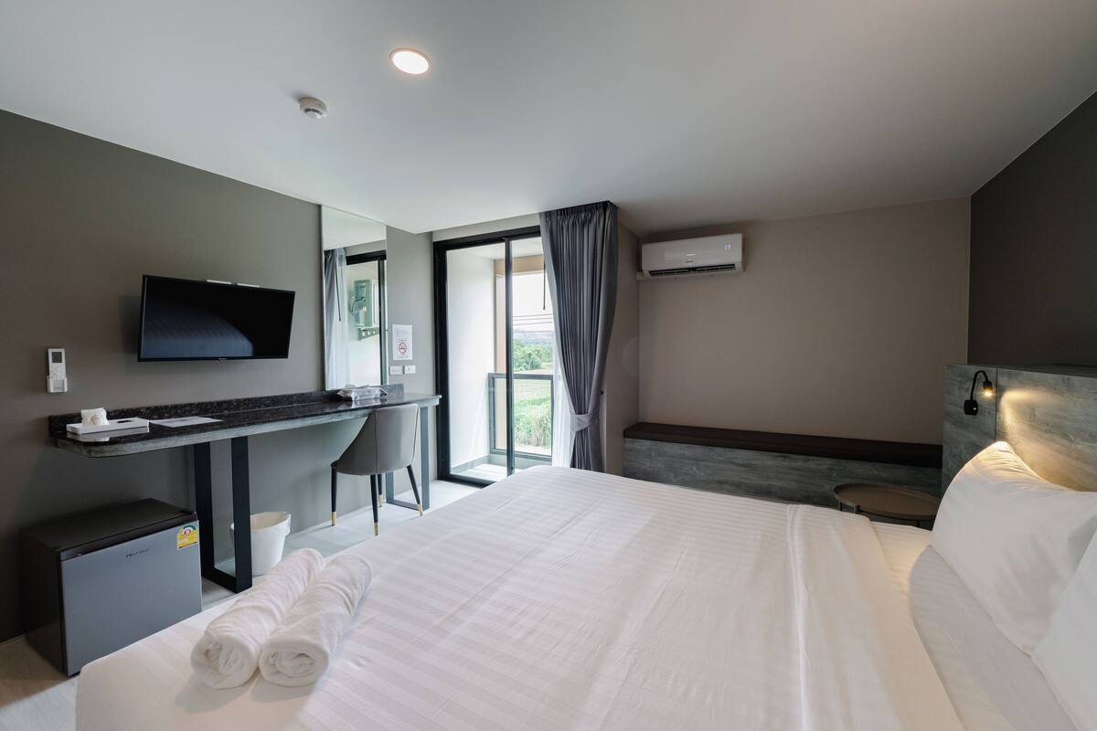A hotel room with a bed, a desk, a television, and a window with curtains.