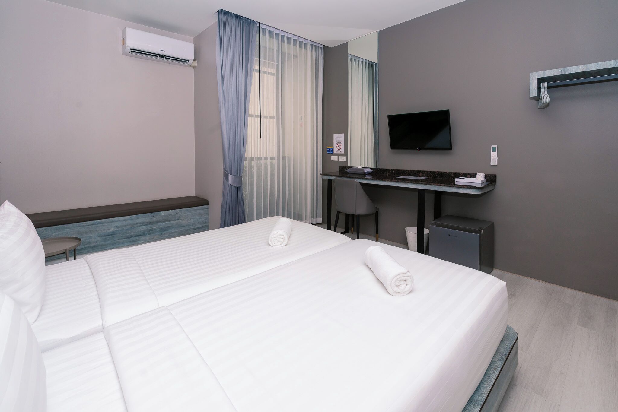 A hotel room with a bed, a desk, a chair, a television, and an air conditioning unit.