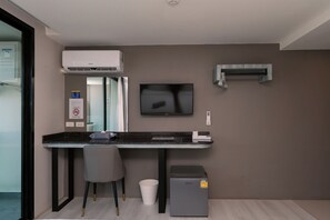 A modern office space with a desk, chair, air conditioning unit, television, and a small cabinet. - One Budget Chiangsaen (Chiang Saen)